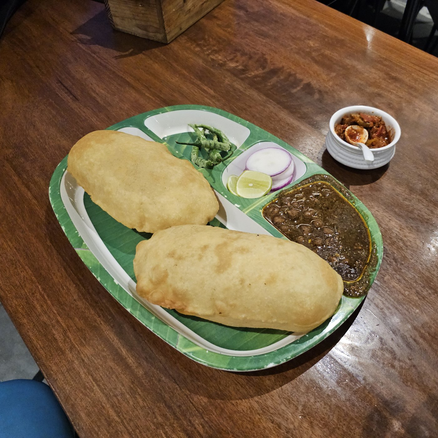 Puffed golden bhature with chole, onion, lime and pickle on a plate.