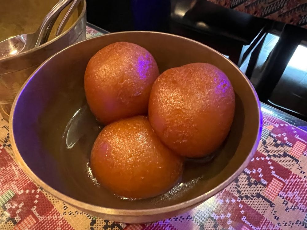 Three golden gulab jamun sweets in a bowl.