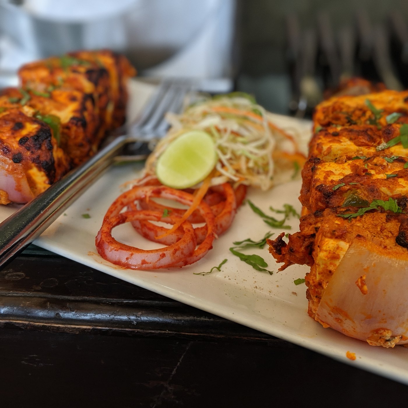 Charred paneer tikka with capsicum, onion and cilantro on a white platter.