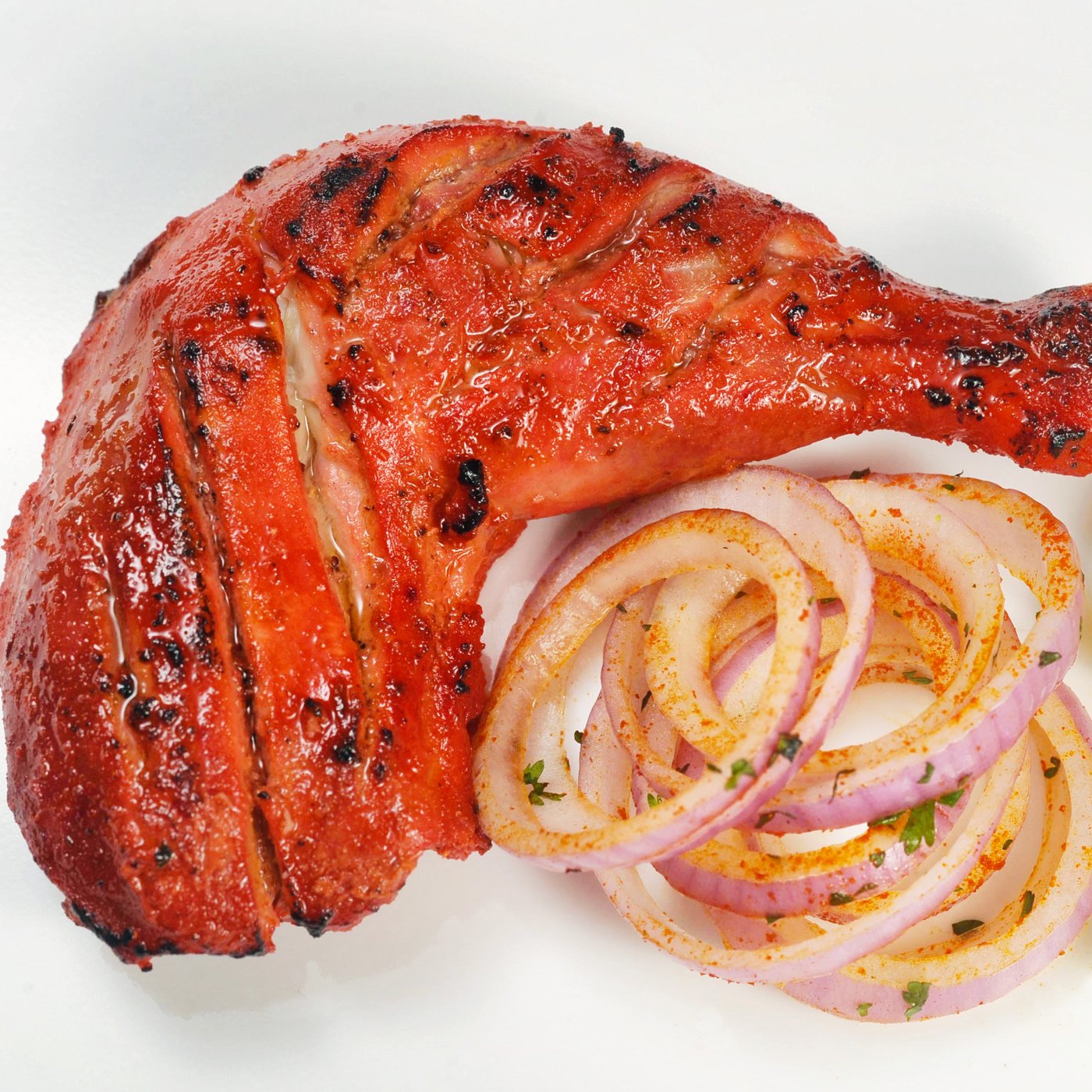 Tandoori chicken with charred skin, sliced onion and lemon wedges.