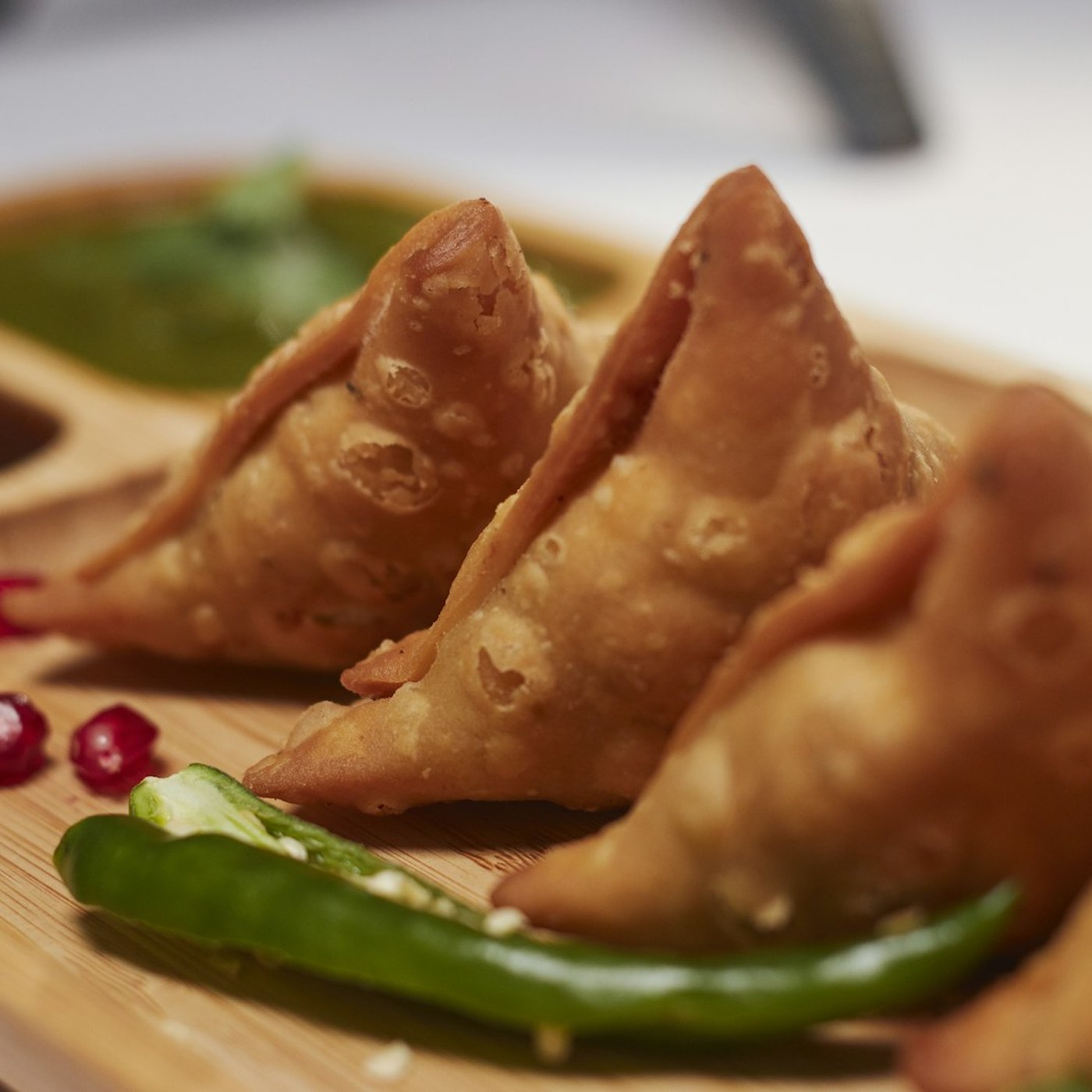 Golden fried vegetable samosas with mint chutney on a wooden platter.