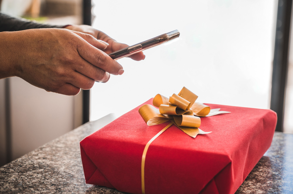 Hands tying a yellow ribbon around a red gift box.