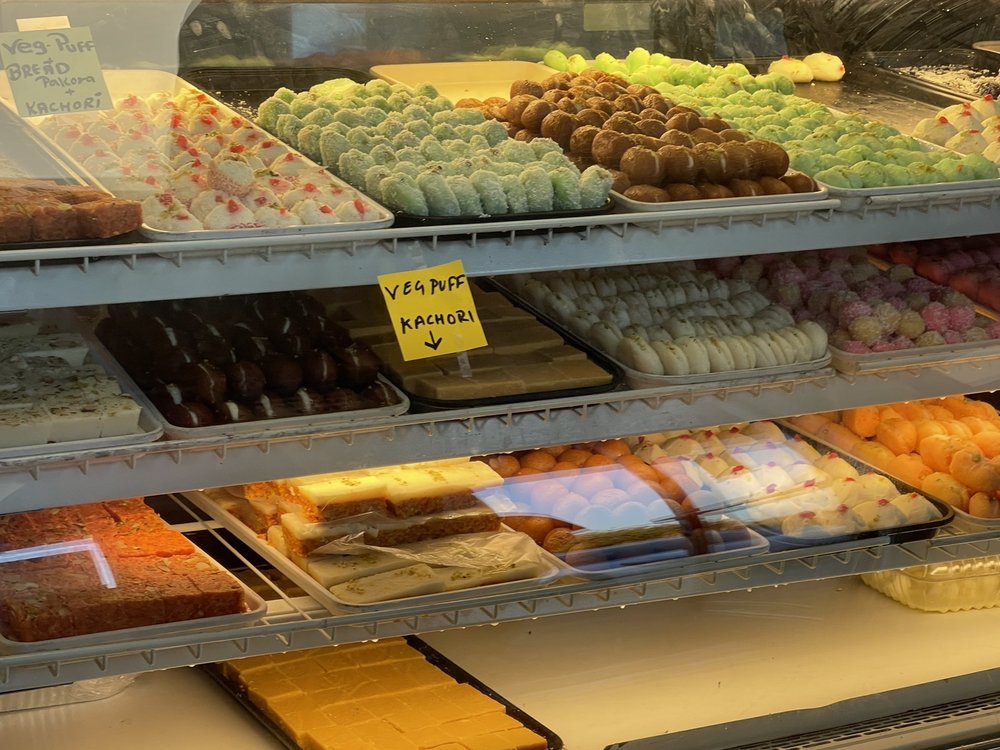 Glass display case filled with trays of Indian mithai at Raja Sweets.